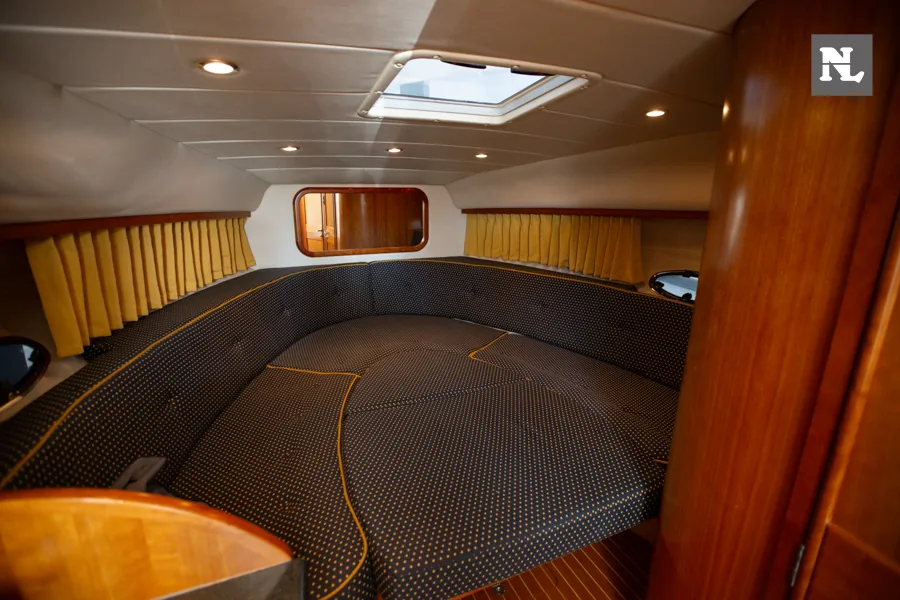 Interior de proa del Windy 32 Scirocco, con litera acolchada, cortinas amarillas, claraboya y acabados de madera.