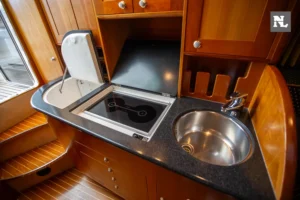 Cocina interior de Windy 32 Scirocco, vista en ángulo con fregadero, placa de cocción y armarios de madera.