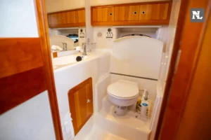 Interior del baño del Windy 32 Scirocco, visto desde la entrada, con inodoro, lavabo y armarios de madera.