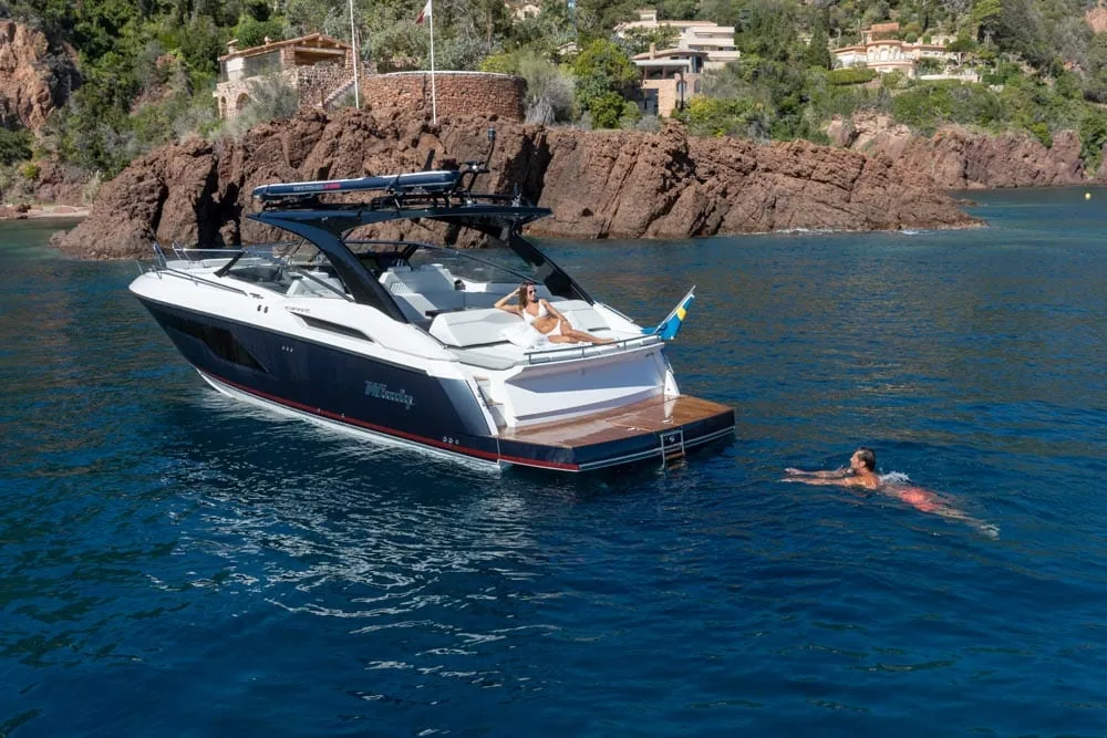 Exterior of the Windy Camira 40 RS anchored by a rocky coast, with a person swimming nearby.
