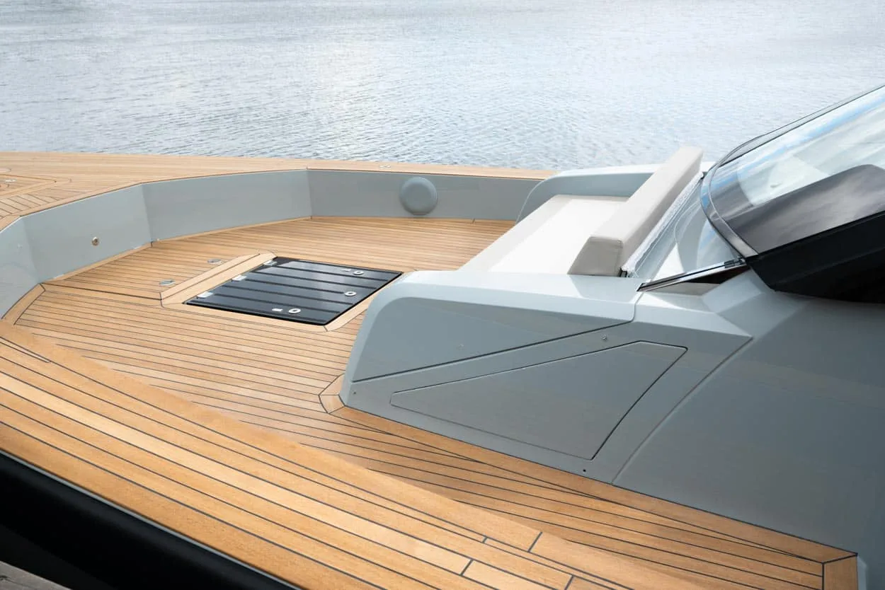 Exterior bow deck of the Windy SR52 Blackbird, with teak flooring, a hatch and a partial windshield by the water