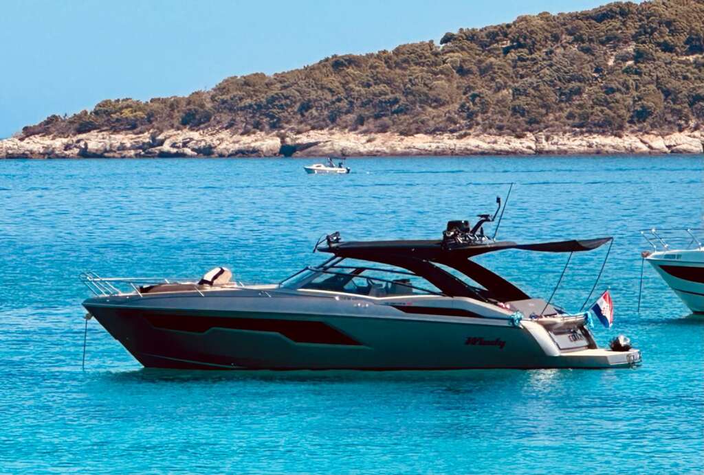 Windy 40 Camira RS visto de estribor, con toldo negro, plataforma de baño y costa rocosa al fondo.